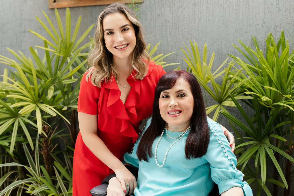 Dra. Fernanda, de vermelho, e Dra. Silvia Roberta, sentada, no jardim da entrada da clínica