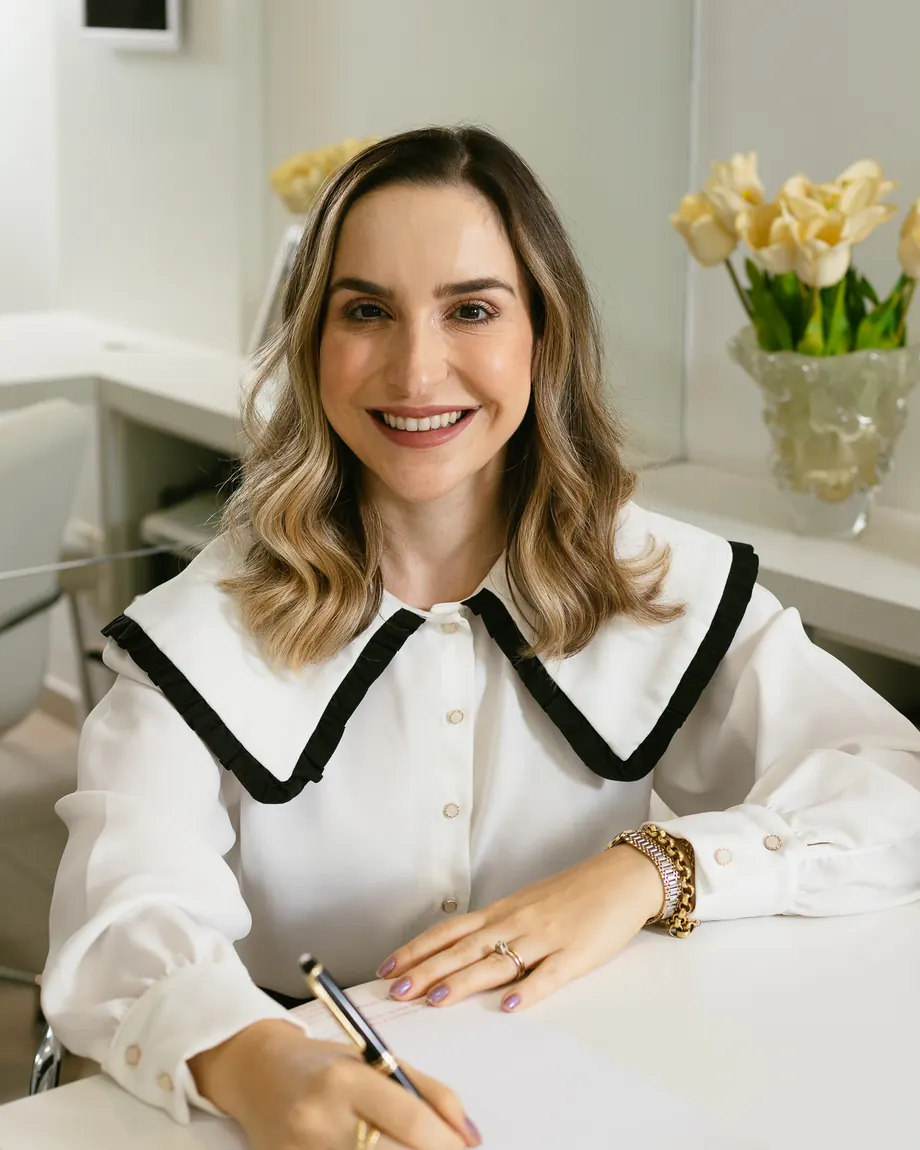Dra. Fernanda Tirelli Rocha escrevendo à mesa do consultório, com um vaso de flores ao lado