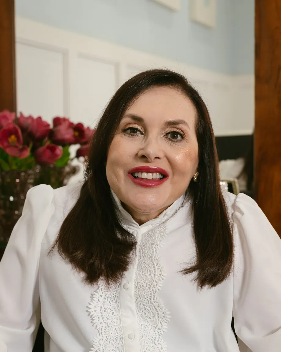 Dra. Silvia Roberta Tirelli Rocha sorrindo no consultório, com um arranjo de flores ao fundo